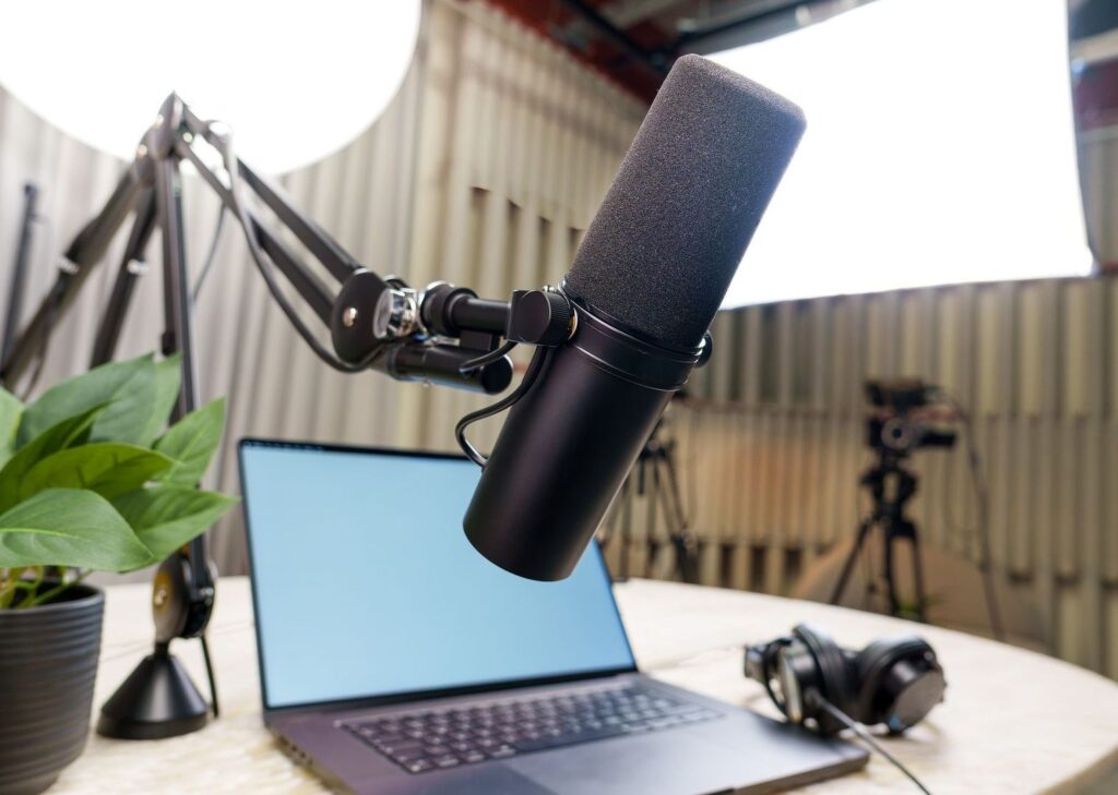 Podcast-studion mikrofoni, kannettava tietokone ja kuulokkeet työpöydällä